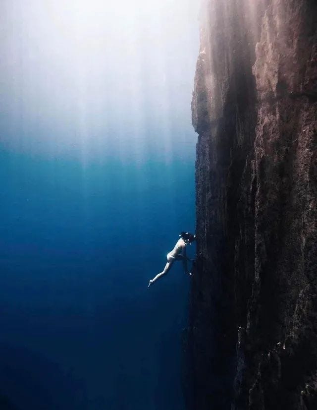 A diver climbing a steep underwater cliff.