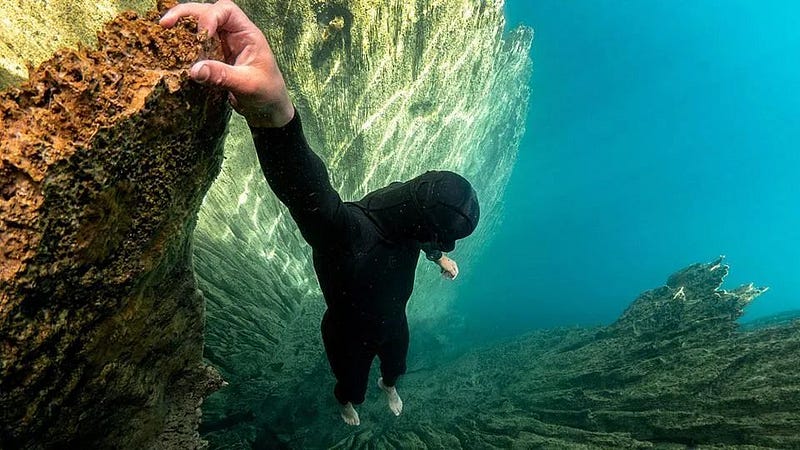 A diver suspended over a deep underwater trench.