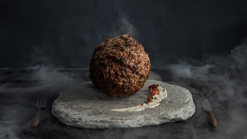 A mammoth meatball beside a knife and fork.